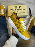 Yellow patterned sneakers with white soles, held by a person, on a wooden floor with a 'Vip Fashion' box in the background.